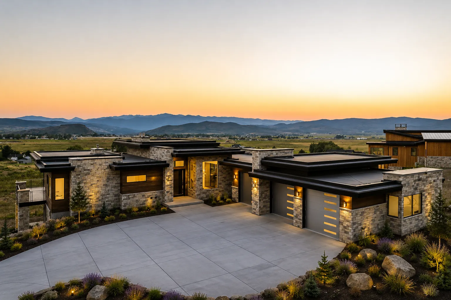 Modern stone-and-timber residence glowing at sunset above a wide mountain valley